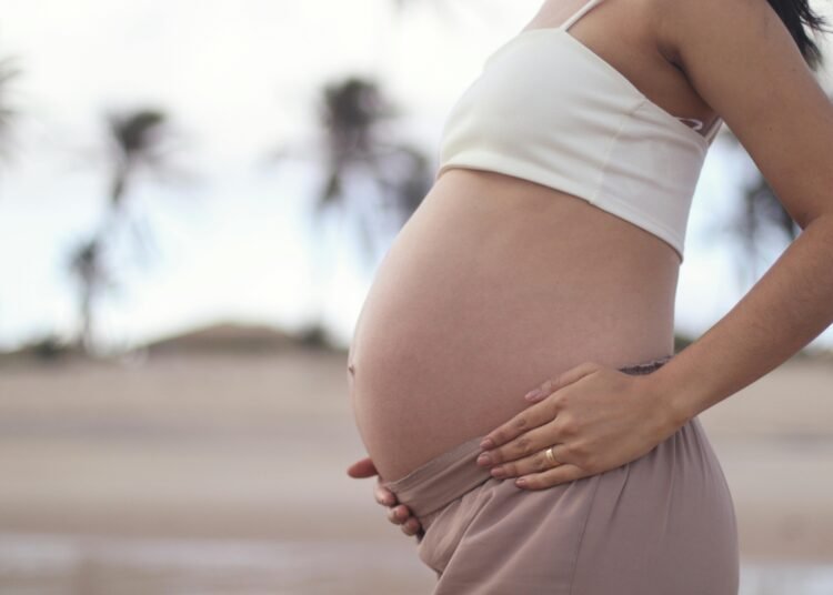 A serene portrait of a pregnant woman holding her belly at a tropical beach.