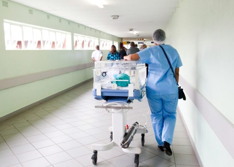 person walking on hallway in blue scrub suit near incubator