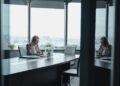 A businesswoman in a blazer works at a desk in a modern office with city views.