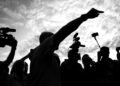 A dramatic silhouette of a media crew with cameras capturing a pointing individual against a cloudy sky.