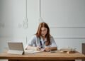 A woman doctor writing notes at a desk with a tablet and books, capturing a professional office setting.