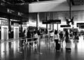 Black and white photo of travelers walking with luggage in a bustling airport terminal.