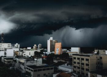 Dramatic storm clouds hover over city skyscrapers, creating a moody urban landscape contrast.