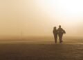 Silhouettes of anonymous elegant ethnic female strolling on arid terrain in dense smog