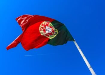 The Portuguese flag waves in the wind against a clear blue sky, symbolizing national pride.