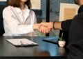a man and a woman shaking hands in front of a laptop