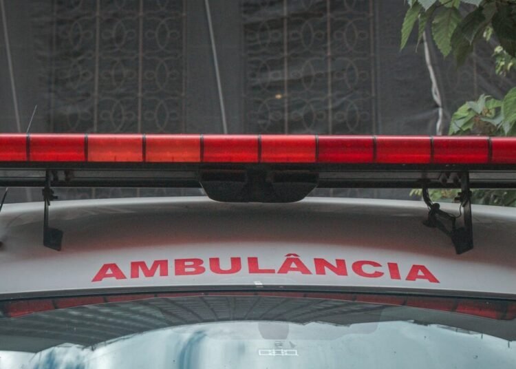 A close-up view of a city ambulance with a red siren light and Portuguese text 'AMBULÂNCIA'