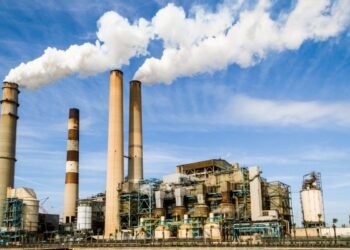 A large industrial power plant with smokestacks emitting smoke under a blue sky, symbolizing pollution.