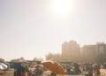 A lively summer beach scene with sunbathers, umbrellas, and distant buildings under a bright sky.