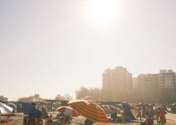 A lively summer beach scene with sunbathers, umbrellas, and distant buildings under a bright sky.
