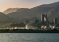 A scenic view of an industrial plant with mountains and water at dusk.