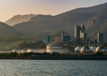 A scenic view of an industrial plant with mountains and water at dusk.