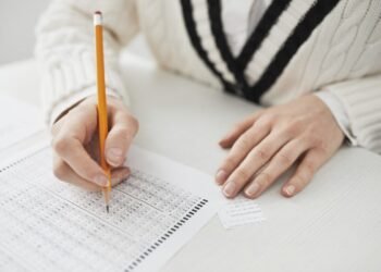A student writing answers on a multiple-choice exam sheet at a desk.