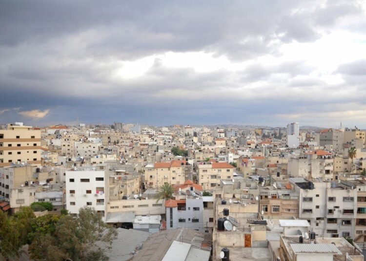 Aerial view of Qalqilya's urban cityscape under dramatic clouds, showcasing diverse architecture.