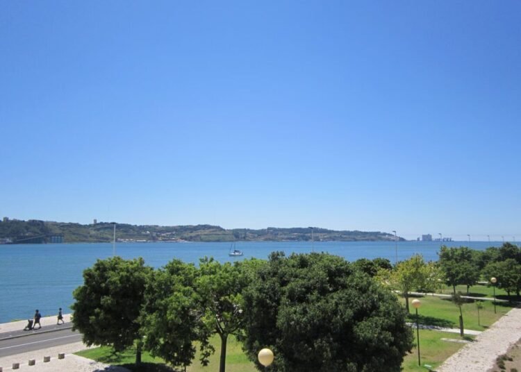 Explore Lisbon's beautiful waterfront with lush greenery and a clear blue sky, perfect for summer strolls.