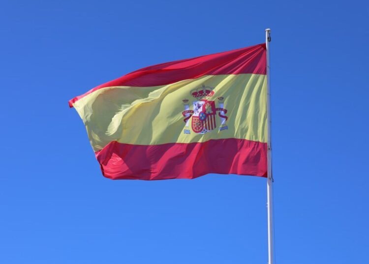 Spanish national flag waving against a clear blue sky in Cádiz, Andalucía.