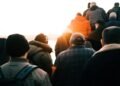 Group of people walking towards the sunrise wearing winter jackets, captured from behind.