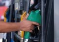 Close-up of a hand holding a green fuel nozzle at a gas pump station outdoors.