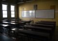 Dimly lit empty classroom featuring rows of desks and whiteboards, creating a contemplative atmosphere.