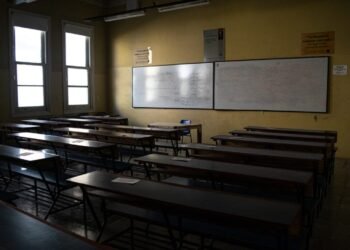 Dimly lit empty classroom featuring rows of desks and whiteboards, creating a contemplative atmosphere.